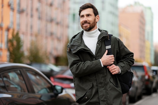 Un hombre sonriente positivo con una mochila en el hombro camina por la calle de la ciudad Un joven camina con confianza al aire libre