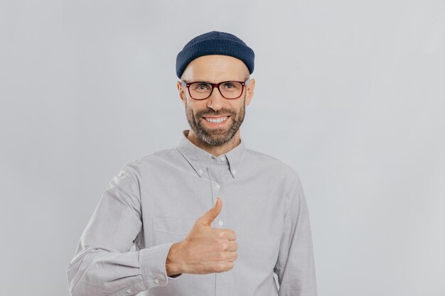 Hombre sonriente positivo con rastrojo levanta el pulgar hacia arriba demuestra su agrado y aprobación usa casco y camisa formal aislado sobre fondo blanco Mi respuesta sí Gesticular Lenguaje corporal