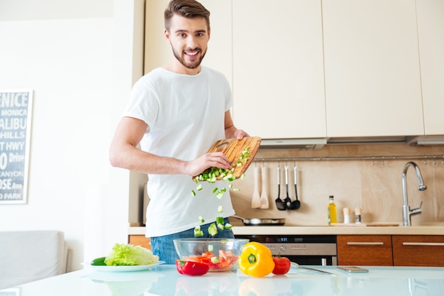 Hombre sonriente preparando ensalada en la cocina