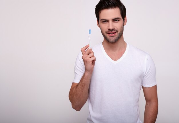 Hombre sonriente que se cepilla los dientes con un cepillo de dientes en blanco.