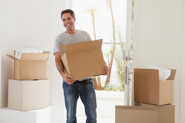 Hombre sonriente que lleva cajas en casa nueva