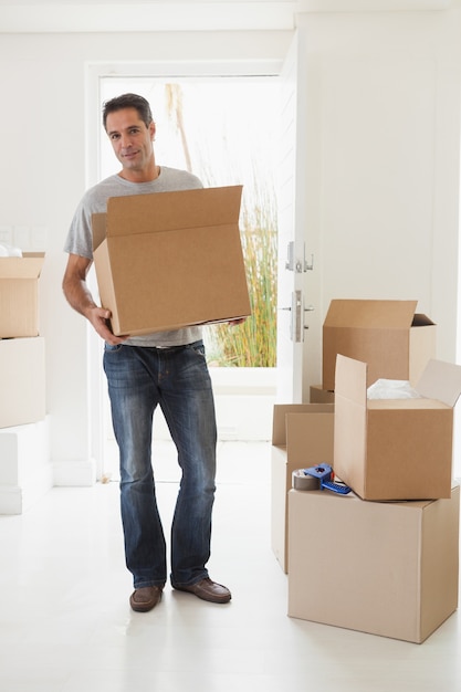 Hombre sonriente que lleva cajas en casa nueva