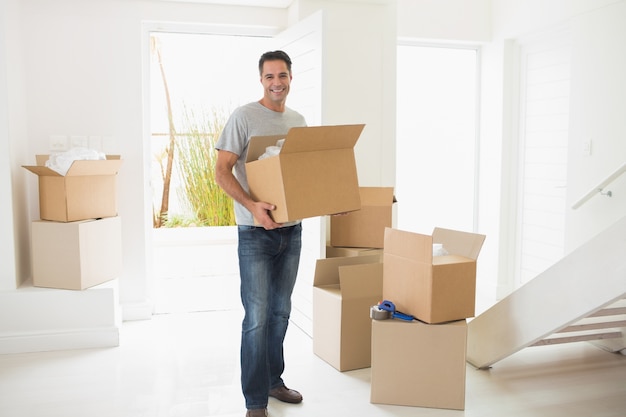 Hombre sonriente que lleva cajas en una casa nueva