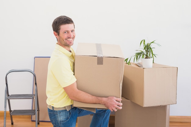 Hombre sonriente que lleva cajas de mudanza de cartón en casa