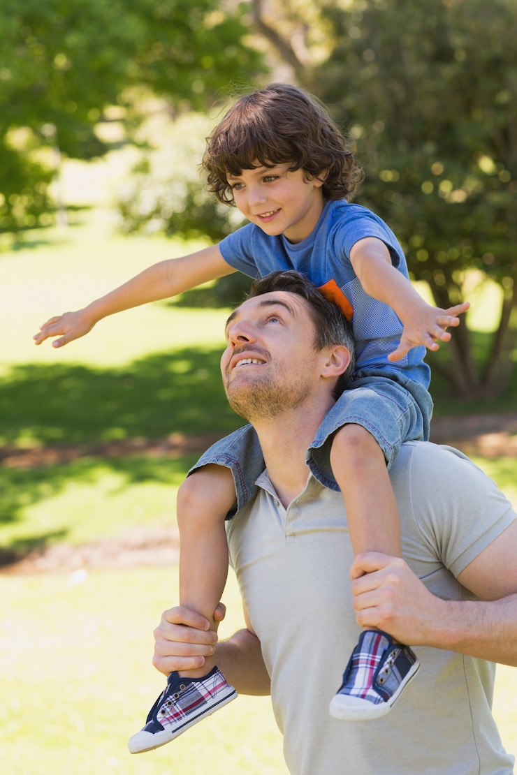 Foto hombre sonriente que lleva a hijo sobre sus hombros en el parque