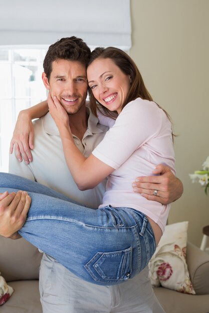 Hombre sonriente que lleva a la mujer en casa