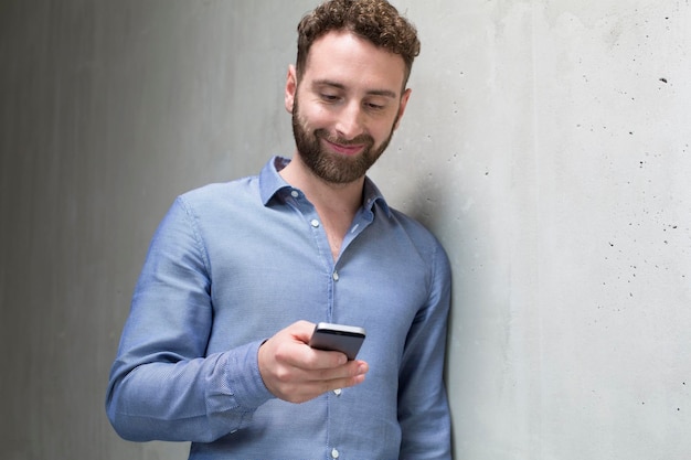 Hombre sonriente que mira el teléfono celular en el muro de cemento