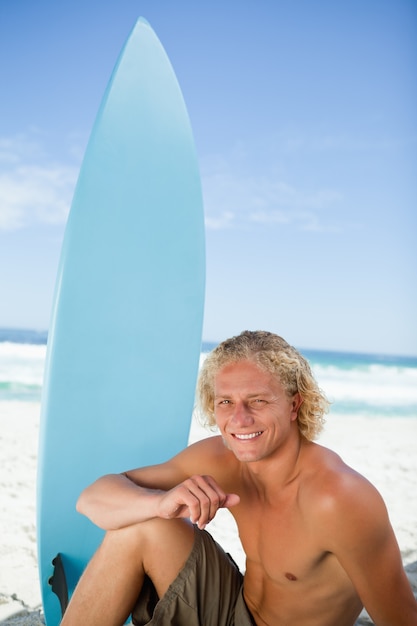 Hombre sonriente que se sienta en la playa con su brazo en su pierna