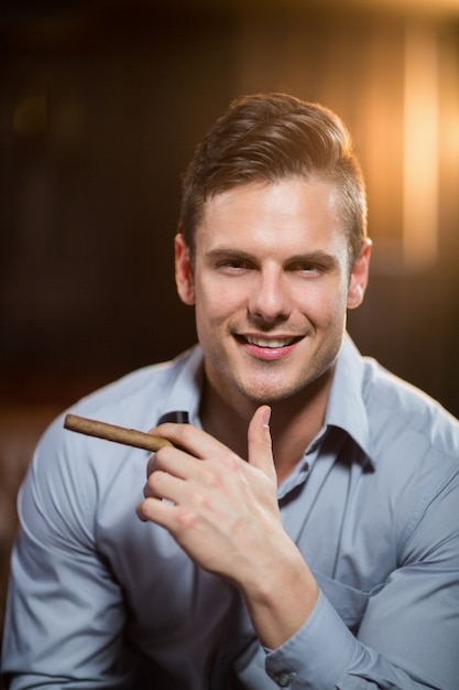 Hombre sonriente que sostiene un cigarro en barra