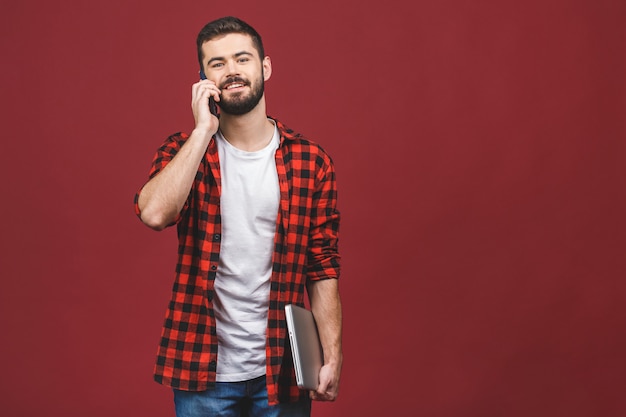 Hombre sonriente que sostiene la computadora portátil en la mano mientras habla por teléfono