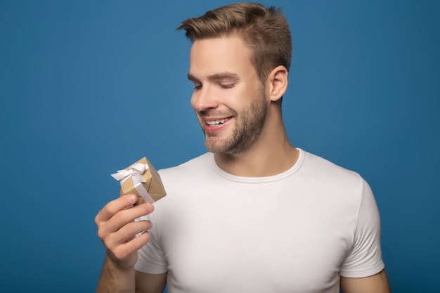 Hombre sonriente que sostiene el pequeño regalo aislado en azul