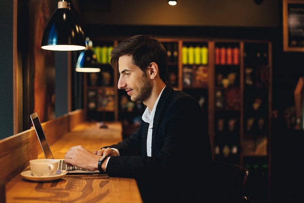 Hombre sonriente que trabaja en la computadora portátil tomando café