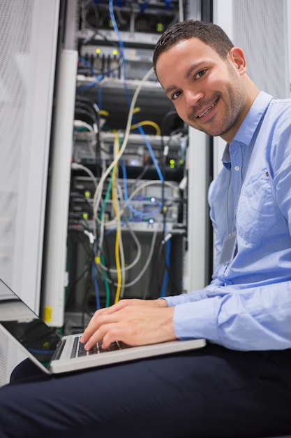 Hombre sonriente que usa la computadora portátil al lado de los servidores