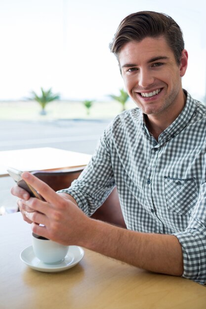 Hombre sonriente que usa su teléfono móvil en cafetería