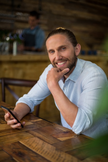 Hombre sonriente que usa el teléfono móvil en café