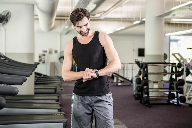 Hombre sonriente en la rueda de ardilla que mira el smartwatch en el gimnasio