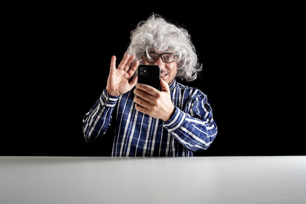 Hombre sonriente sentado en el escritorio con un videochat hablando por teléfono inteligente sobre fondo negro