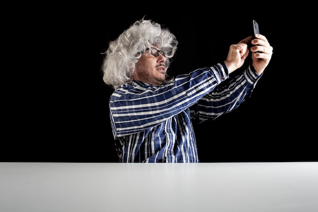 Hombre sonriente sentado en el escritorio con un videochat hablando por teléfono inteligente sobre fondo negro