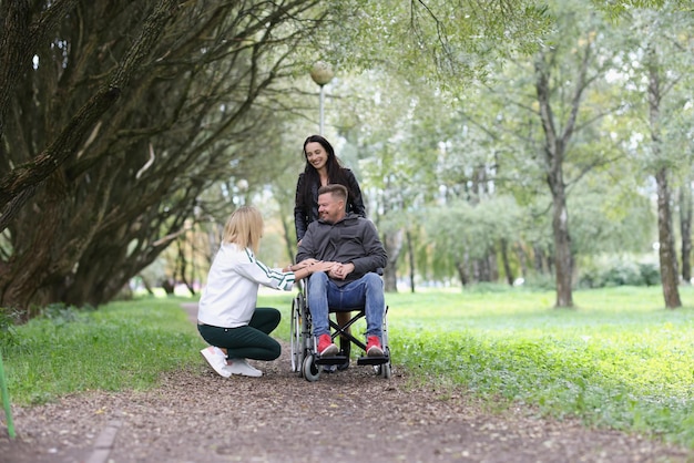 Hombre sonriente en silla de ruedas y dos mujeres se divierten en el parque vida feliz para personas con