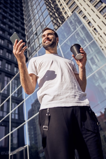 Hombre sonriente con smartphone y café outlook rodillas disparó de cerca