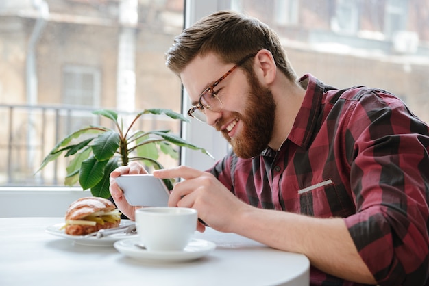 Hombre sonriente con smartphone fotografiando su almuerzo en el café