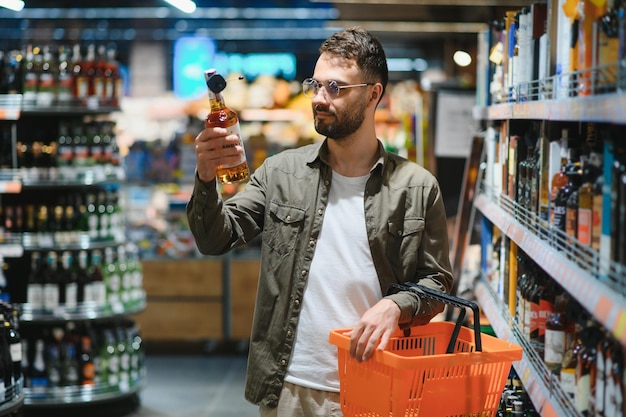 Hombre sonriente sosteniendo una botella de coñac en el supermercado