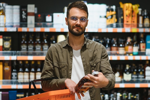 Hombre sonriente sosteniendo una botella de coñac en el supermercado