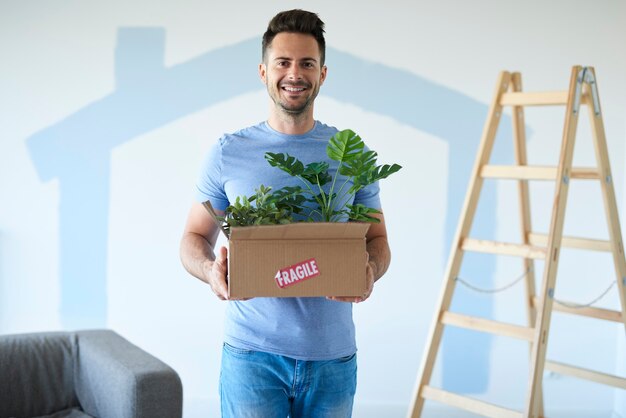 Hombre sonriente sosteniendo caja de plantas en movimiento en casa nueva