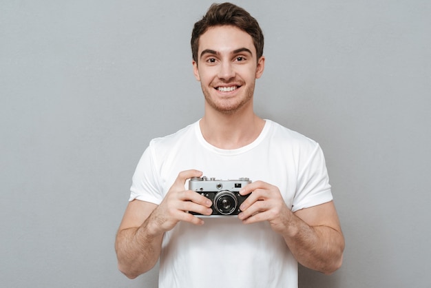 Foto hombre sonriente sosteniendo una cámara retro en las manos. pared gris aislada