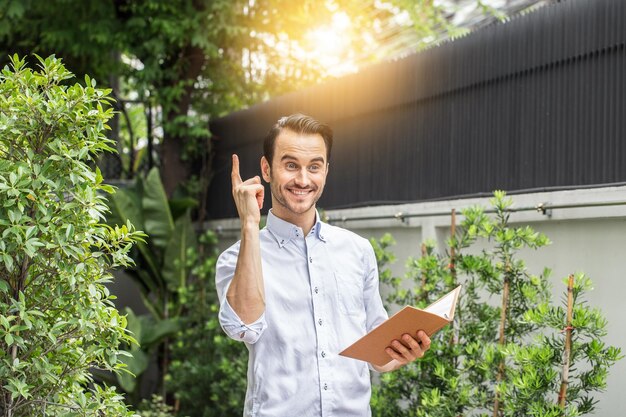 Foto hombre sonriente sosteniendo un cuaderno mientras está de pie al aire libre