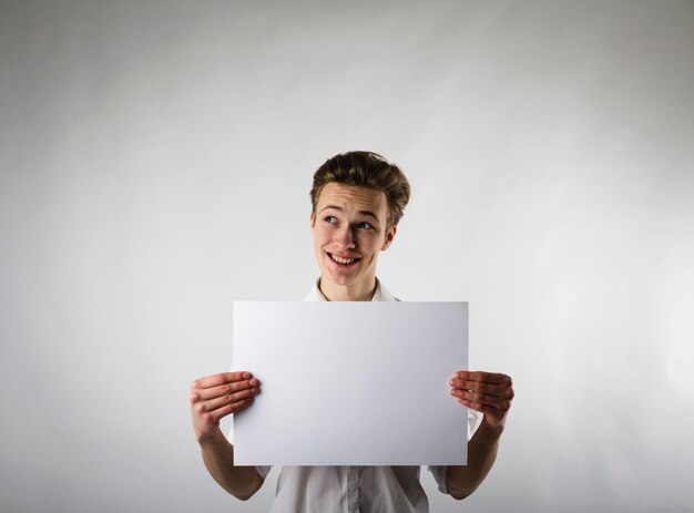 Hombre sonriente sosteniendo un papel en blanco mientras está de pie contra un fondo blanco