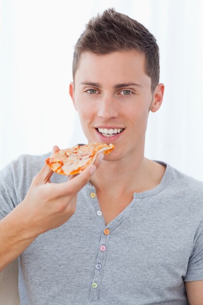 Un hombre sonriente sosteniendo pizza mientras está a punto de comer