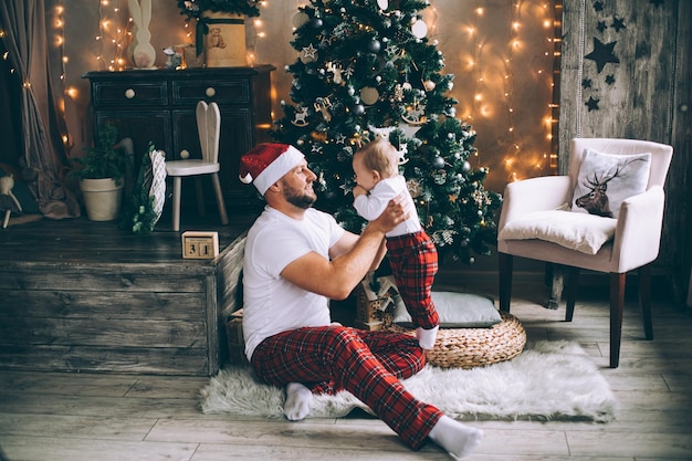 Hombre sonriente sosteniendo a su bebé mientras jugaba cerca del árbol de Navidad