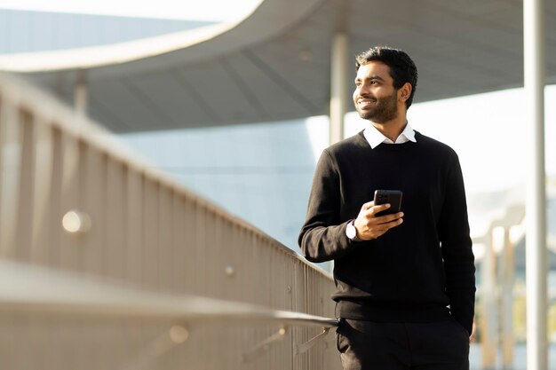 Hombre sonriente sosteniendo un teléfono móvil mirando hacia otro lado en la calle, copiando espacio