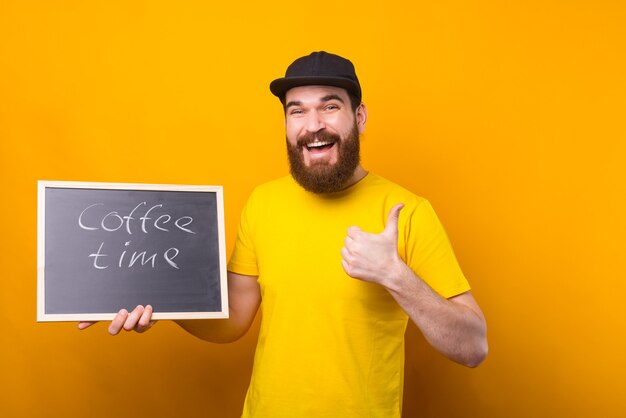 Un hombre sonriente sostiene un tablero negro con la hora del café escrito en él