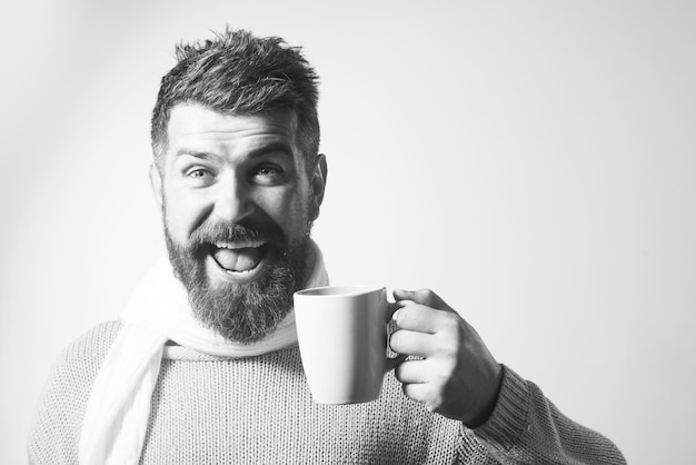 Hombre sonriente en suéter y bufanda disfrutando de una taza de bebidas de la temporada de café y té y el concepto de la gente feliz