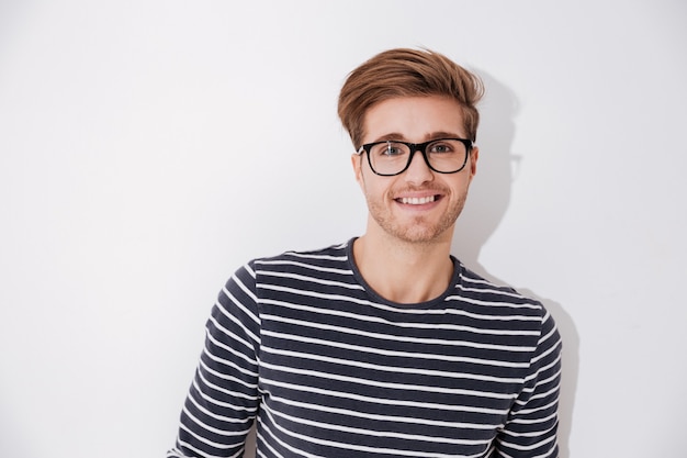 Hombre sonriente en suéter de rayas y gafas mirando a la cámara. Fondo gris aislado