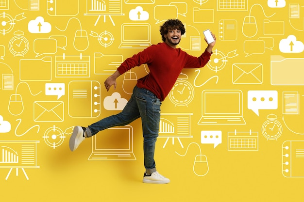 Hombre sonriente con teléfono corriendo sobre diversos íconos del mundo digital