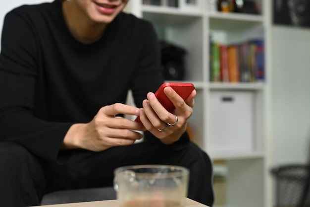 Hombre sonriente de tiro recortado sentado en el sofá y usando teléfonos inteligentes.