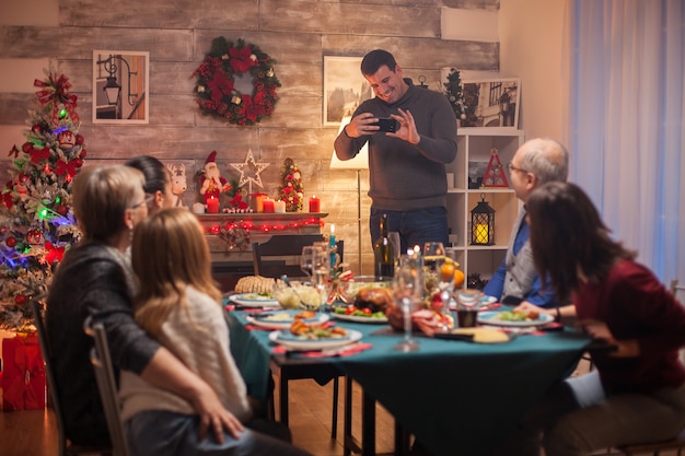 Hombre sonriente tomando fotos de grupo de su familia en la celebración de la Navidad.