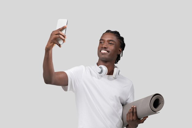 Hombre sonriente tomando una selfie con su teléfono inteligente sobre un fondo blanco