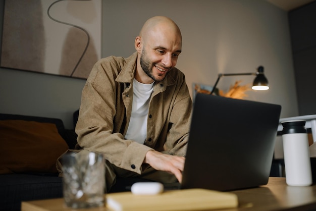 Foto un hombre sonriente está trabajando en una computadora portátil en su apartamento.