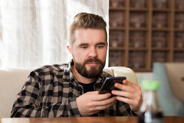 Hombre sonriente usando un teléfono inteligente en una cafetería moderna chateando mensajes en línea en redes sociales móviles