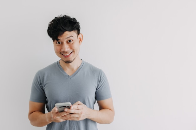 El hombre de la sonrisa está contento con la aplicación de teléfono inteligente aislada en la pared blanca