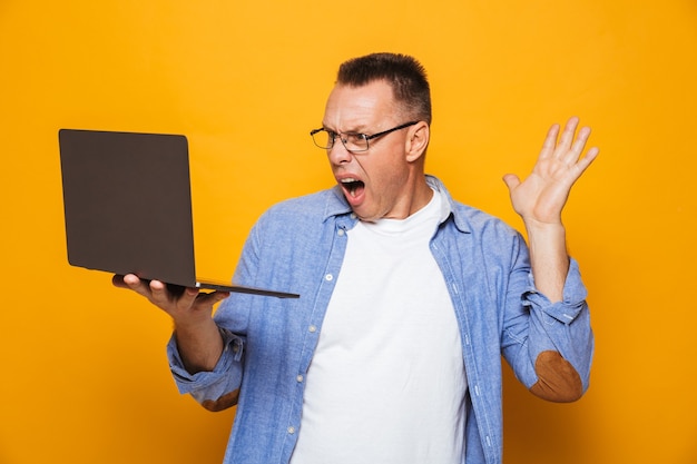 Hombre sorprendido aislado sobre la pared amarilla usando la computadora portátil.