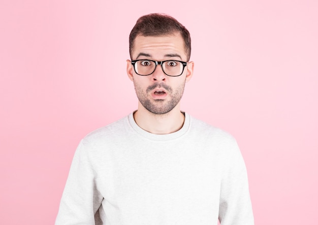 Hombre sorprendido en anteojos con suéter blanco sobre pared rosa