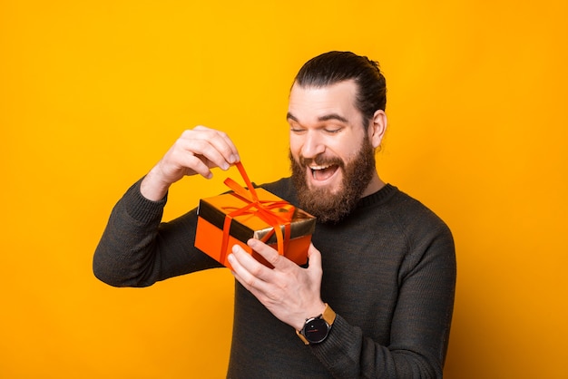 Hombre sorprendido con barba abriendo caja de regalo sobre amarillo