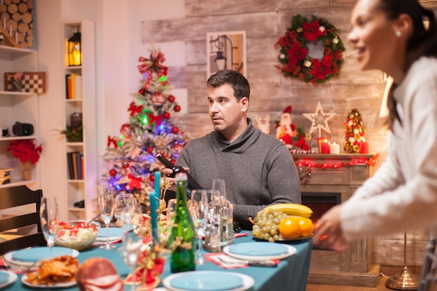 Hombre sorprendido con una botella de vino sentado a la mesa para la cena de Navidad.