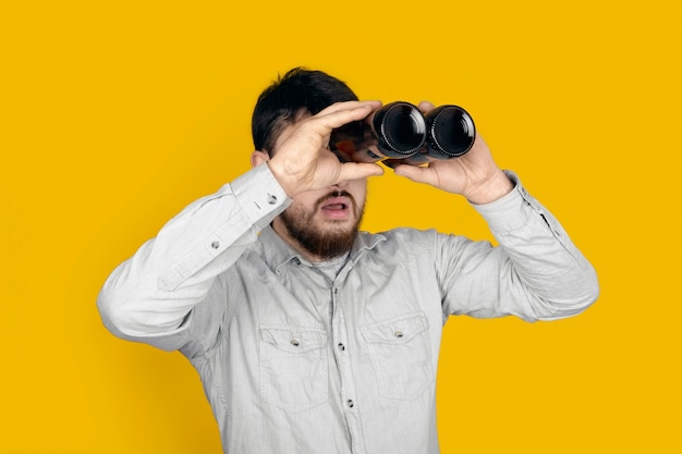 Hombre sorprendido con botellas de cerveza en forma de binoculares sobre pared amarilla