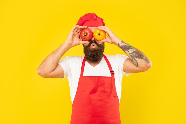 Hombre sorprendido en delantal de cocina y toque sosteniendo tomates en los ojos chef de fondo amarillo